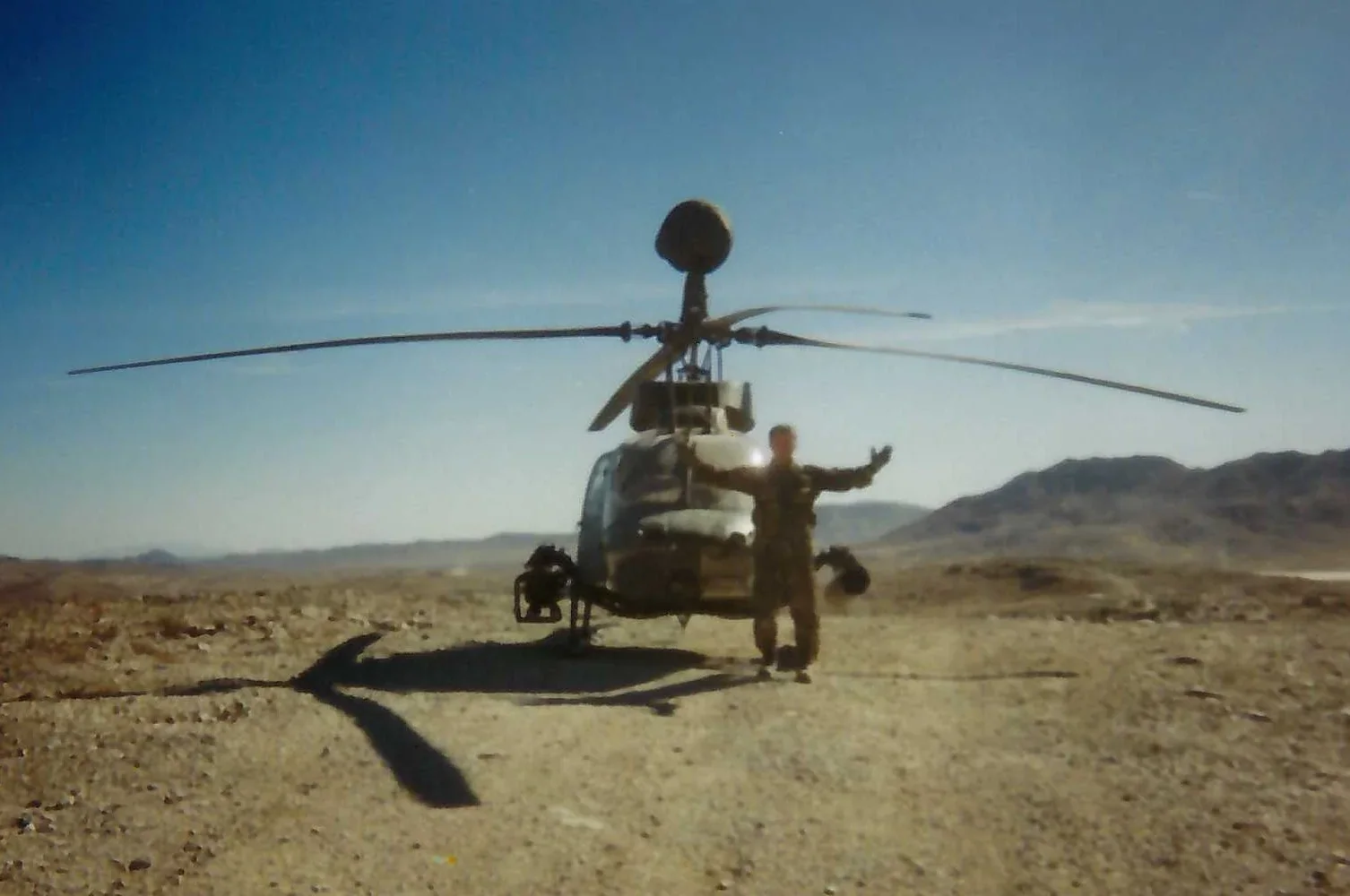 Mike Lewis in uniform, arms spread, standing in front of a helicopter on open desert ground